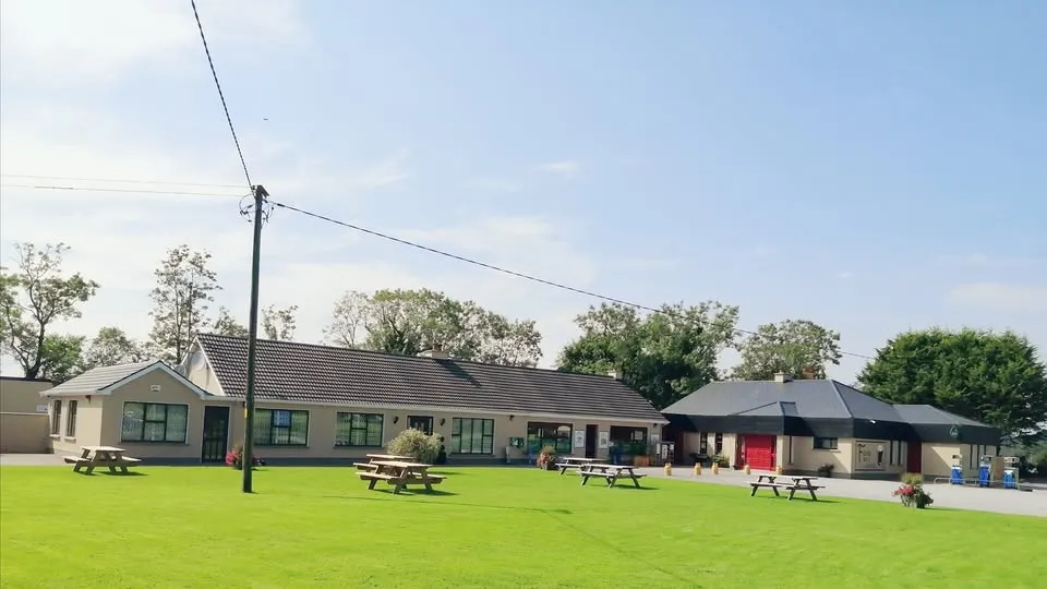 Fox's Bar & Grocery premises in Tooman, Co. Leitrim - cream buildings with grey slate roof, green lawn and wooden picnic tables on a summer day